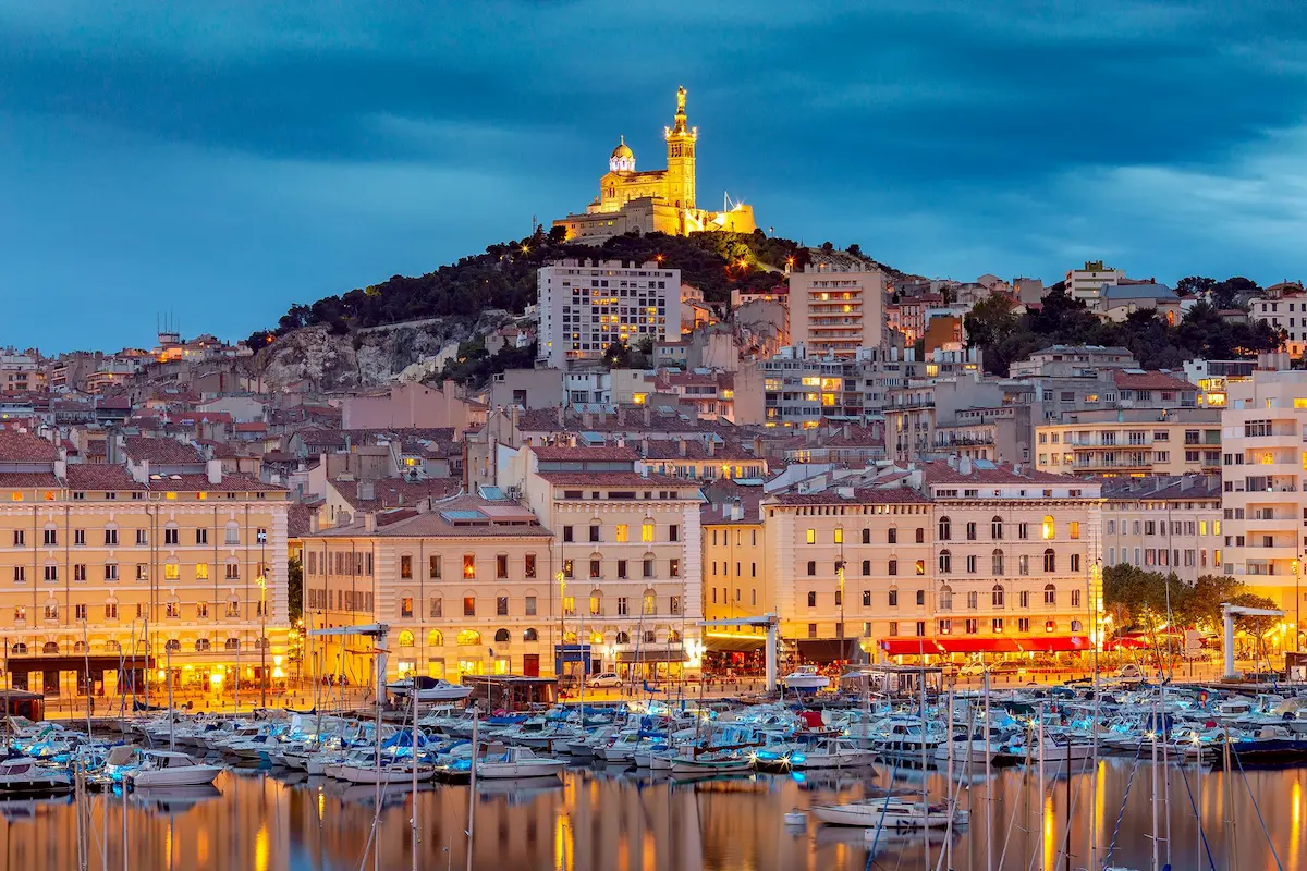 View of Marseille at dusk, port with boats and the illuminated Notre-Dame de la Garde basilica